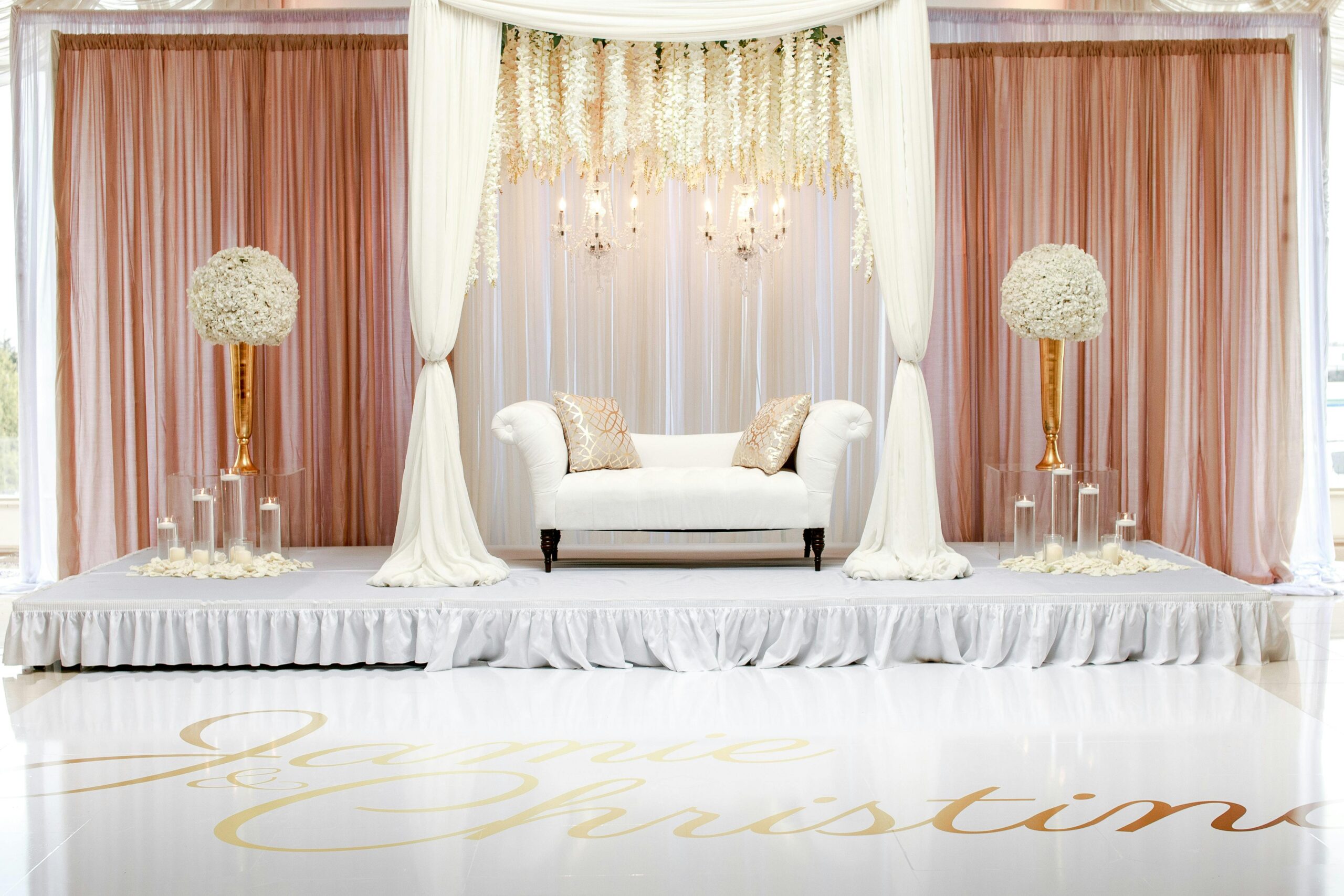 A beautifully styled wedding stage featuring white furniture and floral decorations.
