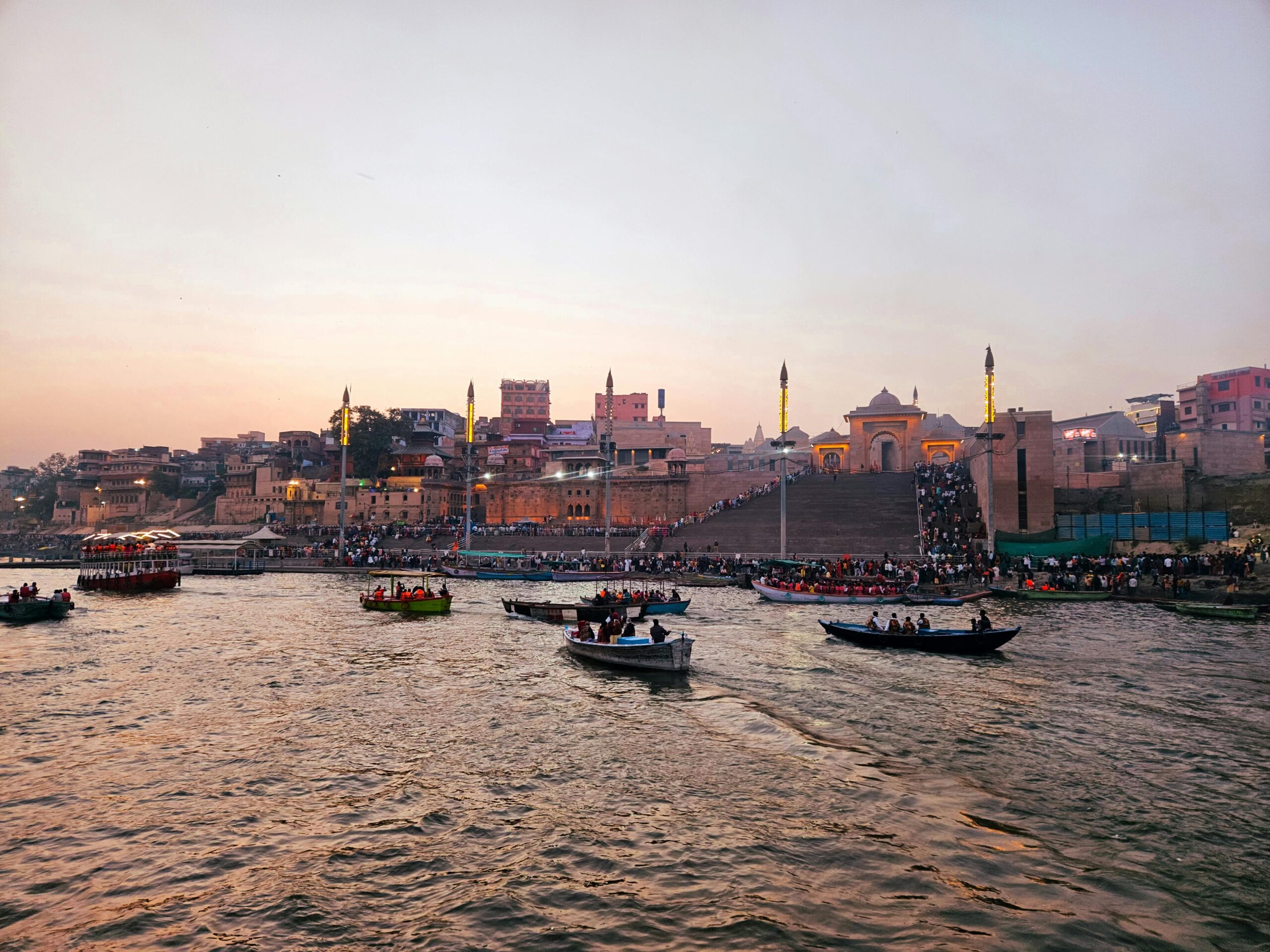 Boats on the Ganges River with Varanasi Ghats at sunset, showcasing Indian cultural heritage.