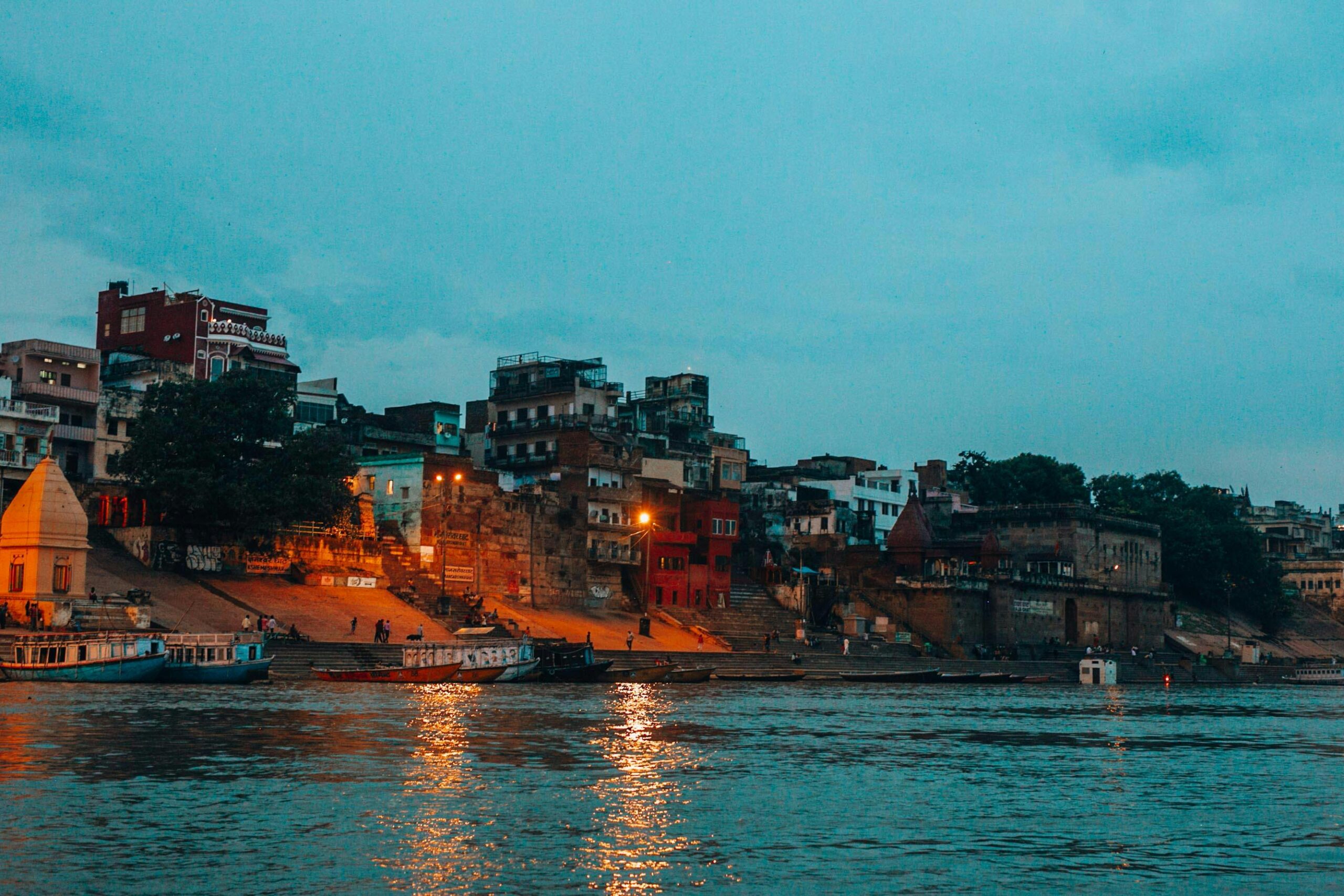 Scenic view of the illuminated Varanasi waterfront along the Ganges River at twilight.